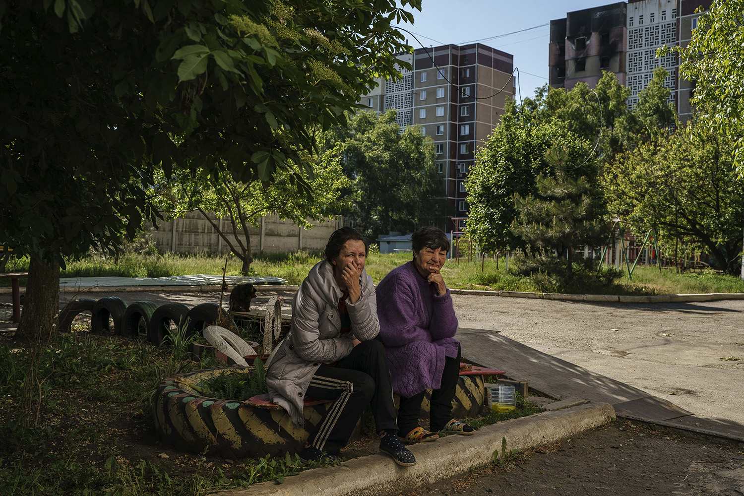 Dos mujeres descansan a la sombra frente a un bloque residencial incendiado el 25 de mayo.