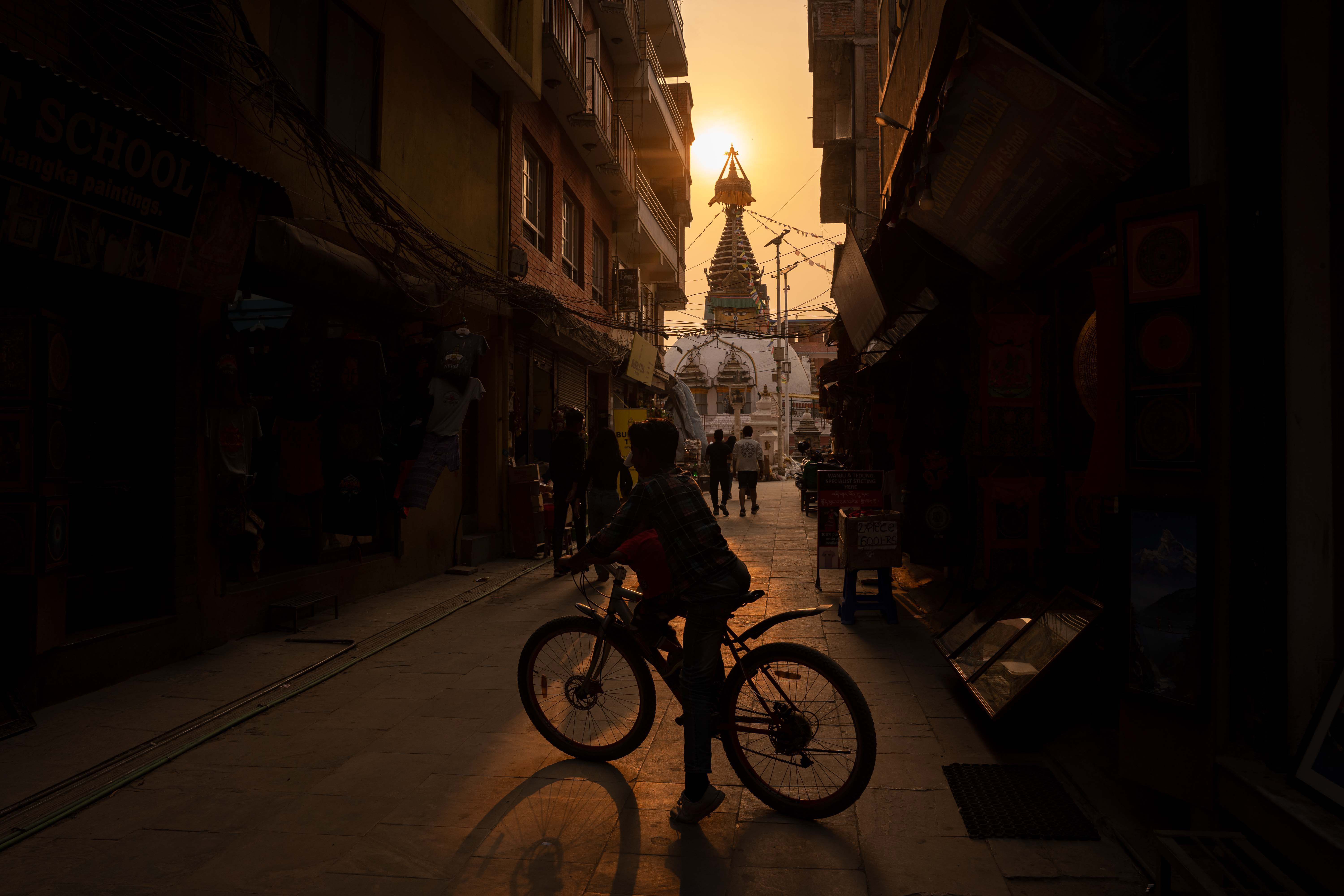 Dos niños montan en bicicleta en un estrecho callejón vacío mirando hacia una estupa budista el 23 de junio. La urbanización incontrolada ha congestionado Katmandú con pocos o ningún espacio abierto.