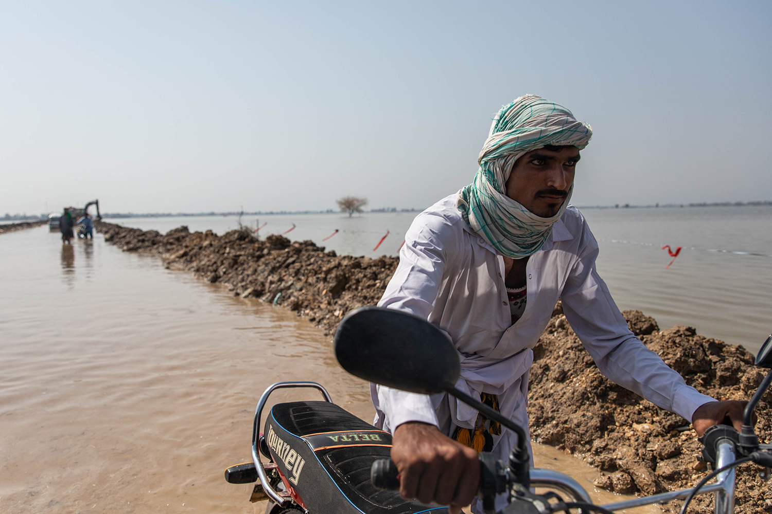 Un hombre empuja su moto a través de un tramo de carretera inundado en Pakistán.