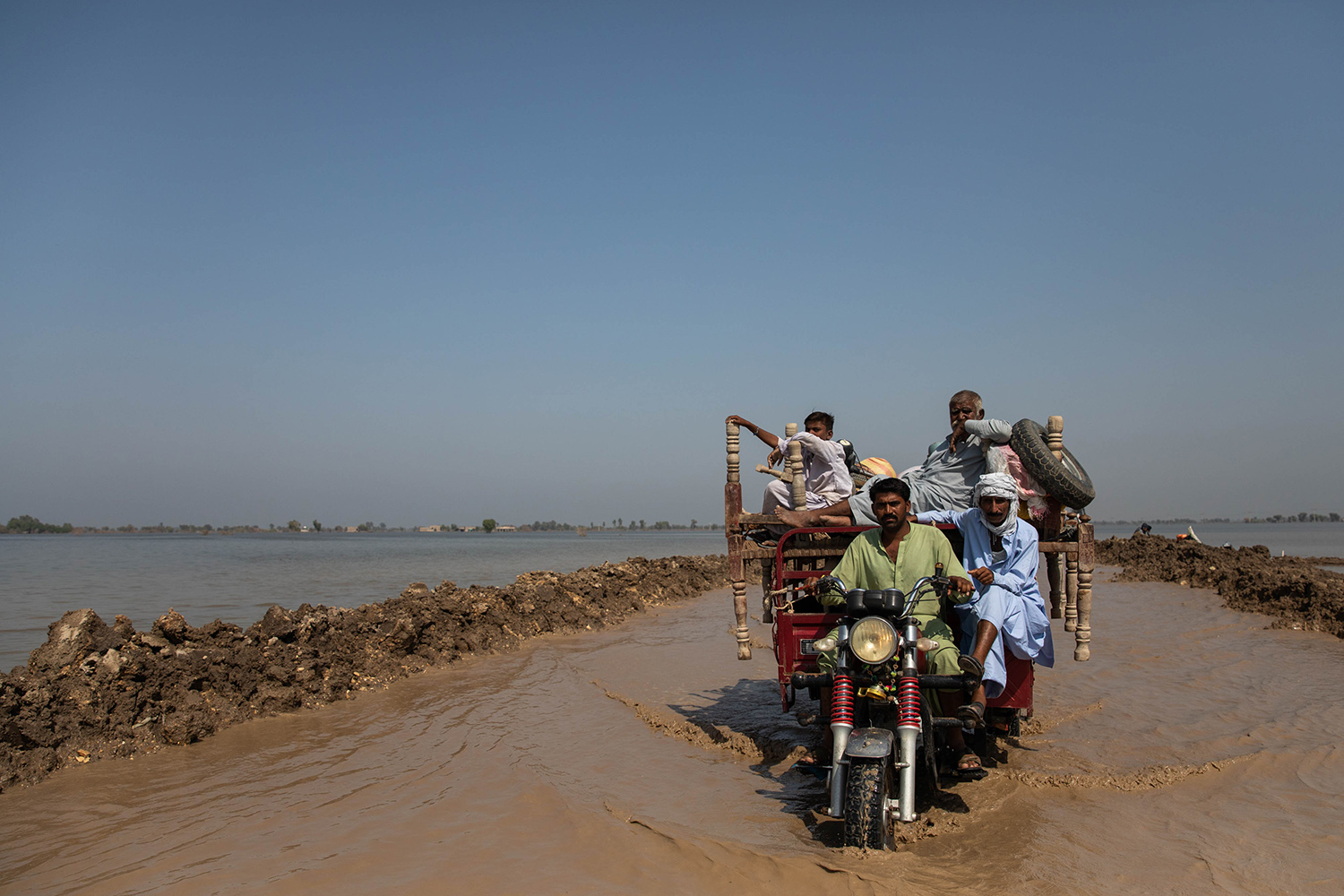 Un carro que transporta hombres y muebles se abre paso por una carretera inundada en Paksitan.
