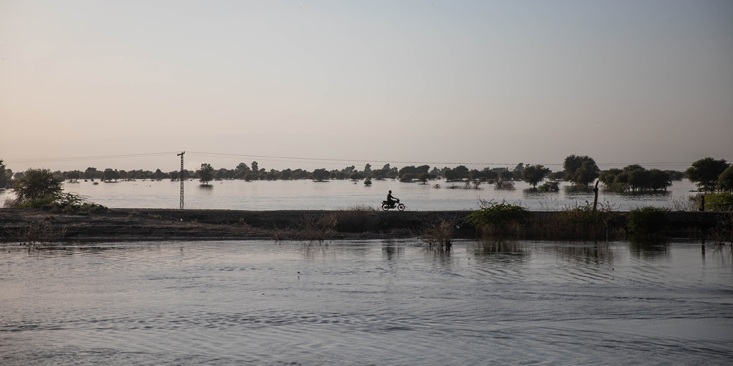 Una motocicleta cruza un terraplén rodeado por las aguas de la inundación en Pakistán.