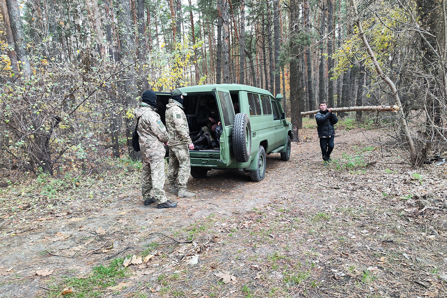Un hombre recoge leña mientras el SBULos oficiales interrogan a un hombre cerca de la línea del frente ruso en la provincia de Kharkiv, Ucrania.