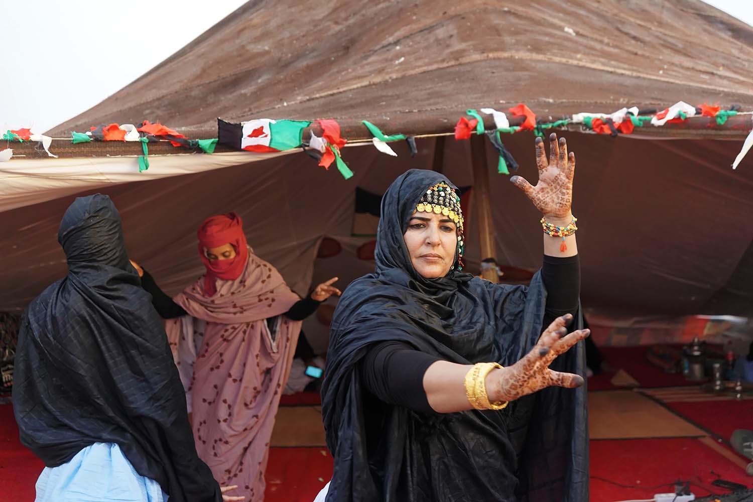 Mujeres saharauis actúan fuera de una tienda tradicional con banderas del Sahara Occidental en el campamento de Auserd como parte del festival FiSahara en el Sahara Occidental.