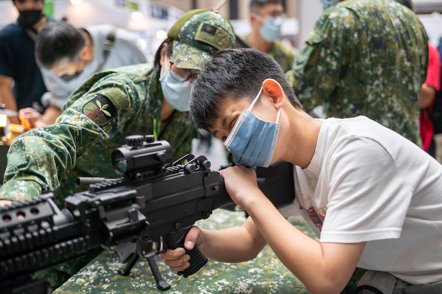 Un miembro de las fuerzas armadas muestra una ametralladora ligera descargada a un niño de primaria en una campaña de reclutamiento de la Academia Militar en la feria de airsoft MOA en Taipei, Taiwán, el 4 de diciembre.