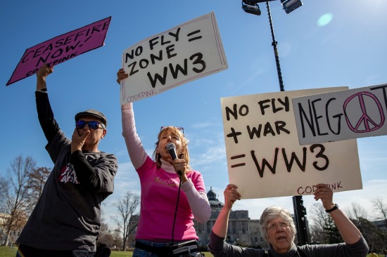 Los manifestantes sostienen carteles que dicen "No-Fly Zone = WW3" y "Alto el fuego ahora."